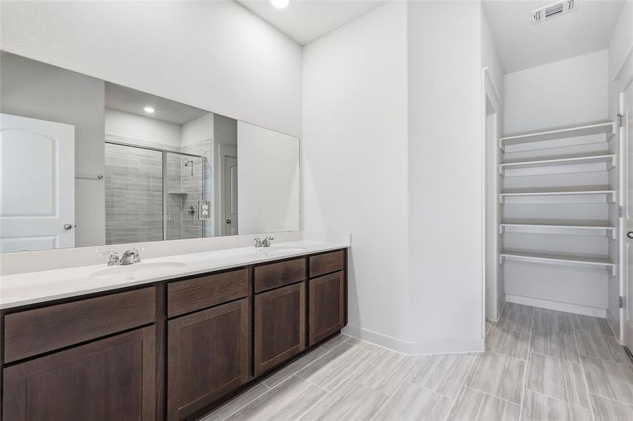 Bathroom featuring a dual vanity with dark wood-finish cabinetry and white countertops, a large wall-mounted mirror, and tile flooring
