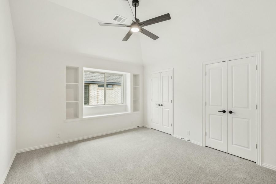 Empty bedroom with vaulted ceiling, ceiling fan, built-in shelves, and double doors with carpet flooring Empty bedroom with vaulted ceiling, ceiling fan, built-in shelves, and double doors with carpet flooring