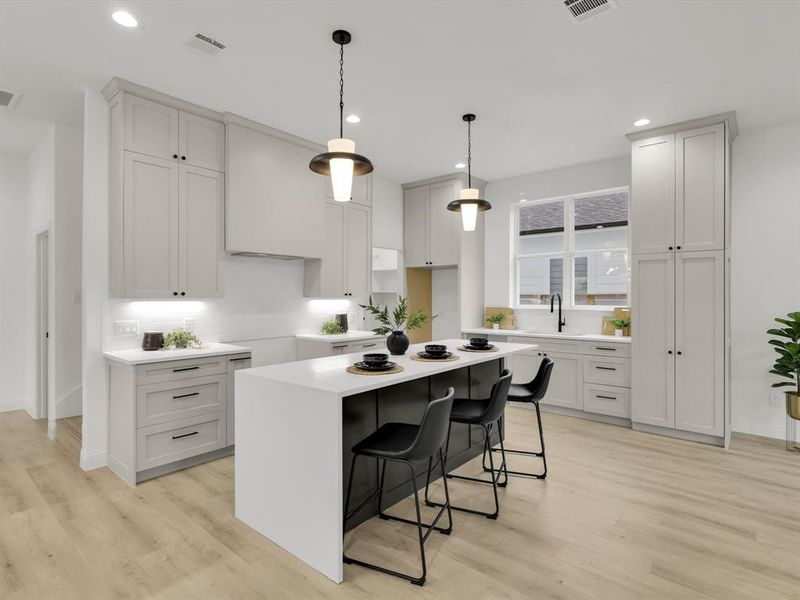 Kitchen with sink, a kitchen breakfast bar, pendant lighting, light hardwood / wood-style floors, and a kitchen island