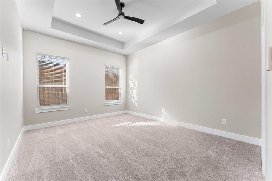 Spare room featuring light carpet, a tray ceiling, and ceiling fan