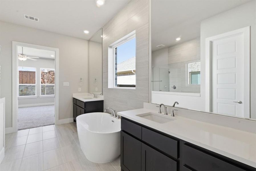 Full bath featuring a soaking tub, two vanities, a shower stall, tile walls, and light tile patterned floors