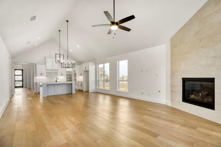 Unfurnished living room with a high ceiling, a tiled fireplace, light wood-style flooring, healthy amount of natural light, and a chandelier