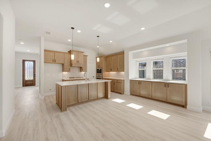 Open kitchen with light wood cabinets, center island, tile backsplash, and light hardwood floors