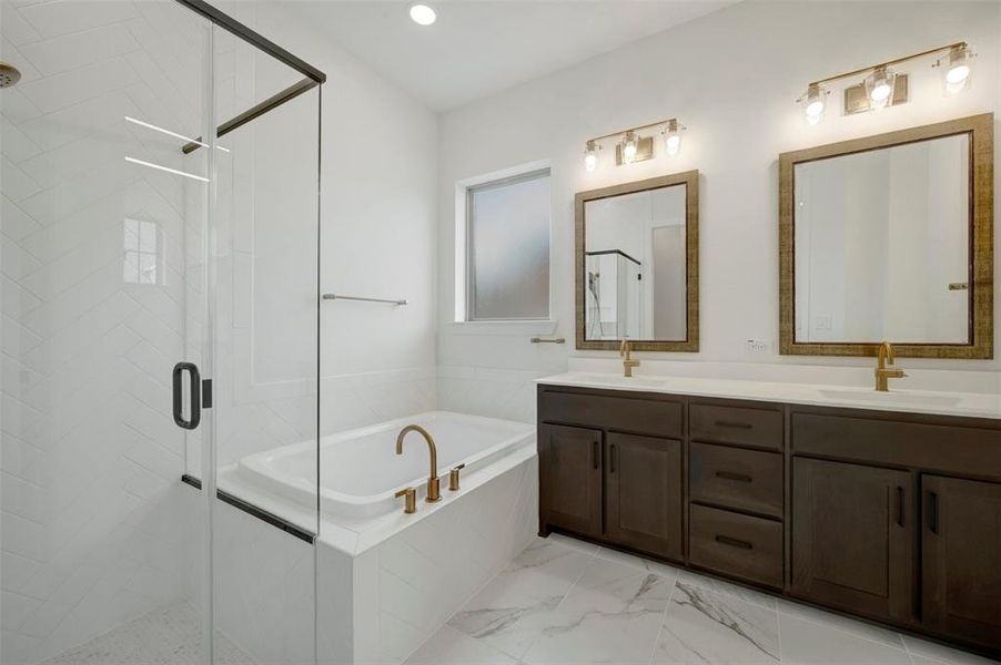 White bathroom featuring a glass-enclosed shower, a built-in soaking tub with a bronze faucet, a double vanity with dark wood cabinetry, and framed mirrors with overhead lighting