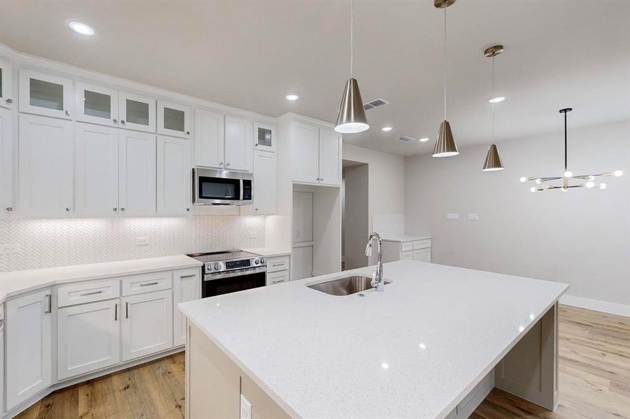 Kitchen featuring white cabinetry, pendant lighting, an island with sink, and stainless steel appliances