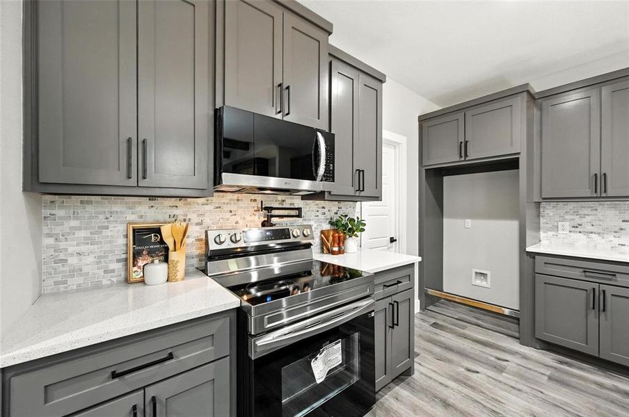 Kitchen with gray cabinets, appliances with stainless steel finishes, backsplash, and light stone counters Kitchen with gray cabinets, appliances with stainless steel finishes, backsplash, and light stone counters