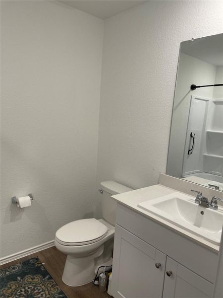 Full bathroom with a textured wall, dark wood-type flooring, vanity, and a shower