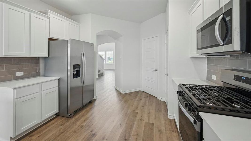 Contemporary kitchen featuring white cabinetry, light countertops, stainless steel appliances, and a subway tile backsplash