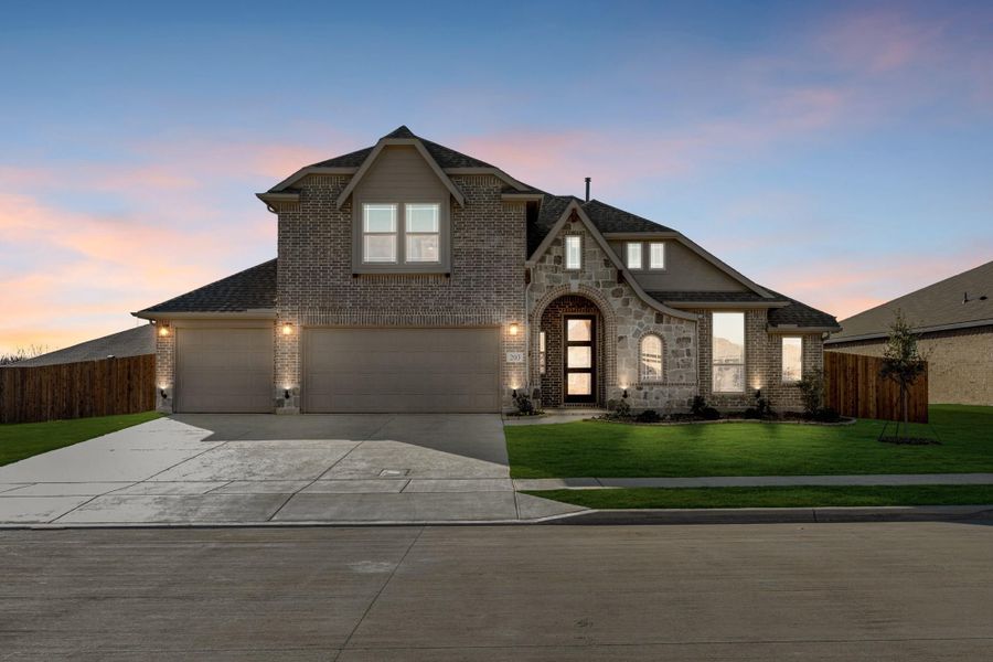 Two-story brick and stone home with two-car garage, arched entry, and green lawn at dusk