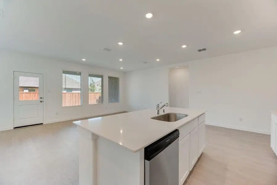 Kitchen with light wood-style floors, dishwasher, light countertops, white cabinetry, and a kitchen island with sink