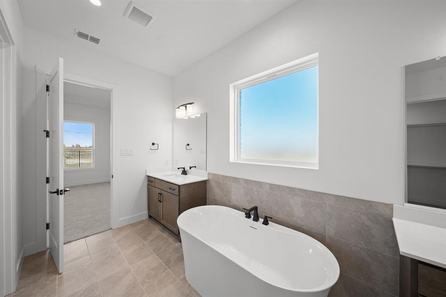 Full bath featuring a freestanding bath, vanity, tile walls, light tile patterned flooring, and a wainscoted wall