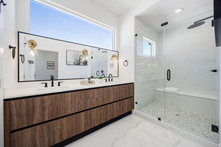 Luxurious primary bath featuring elegant marble finishes, a spacious glass-enclosed shower with bench, and a double vanity with ample storage.
