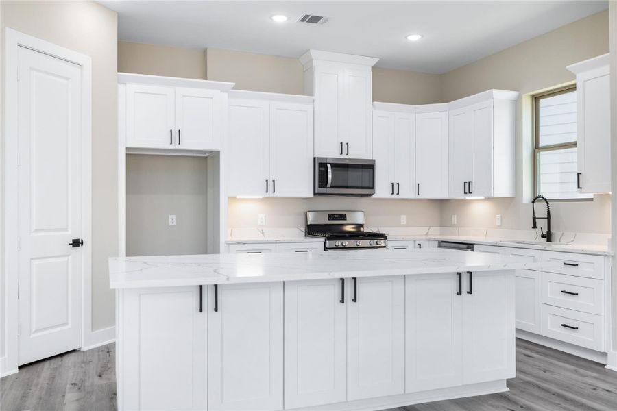 The modern kitchen features sleek white cabinetry and stainless steel appliances with a spacious granite countertop island. With