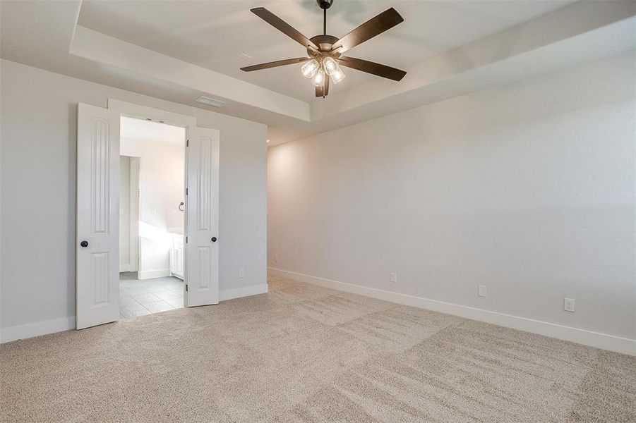 Empty room with a raised ceiling, ceiling fan, and light colored carpet