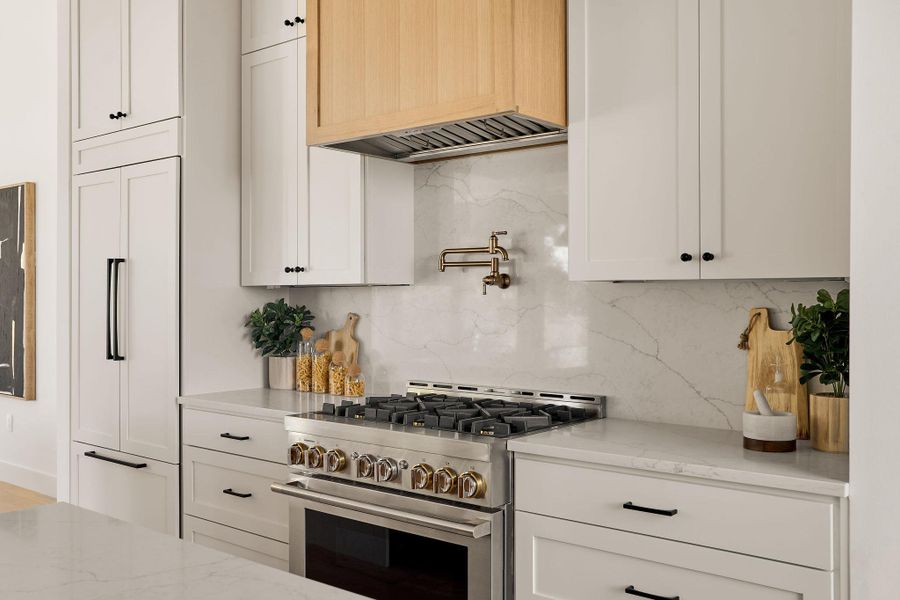 Kitchen with high end stainless steel range, tasteful backsplash, light stone counters, and white cabinetry Kitchen with high end stainless steel range, tasteful backsplash, light stone counters, and white cabinetry