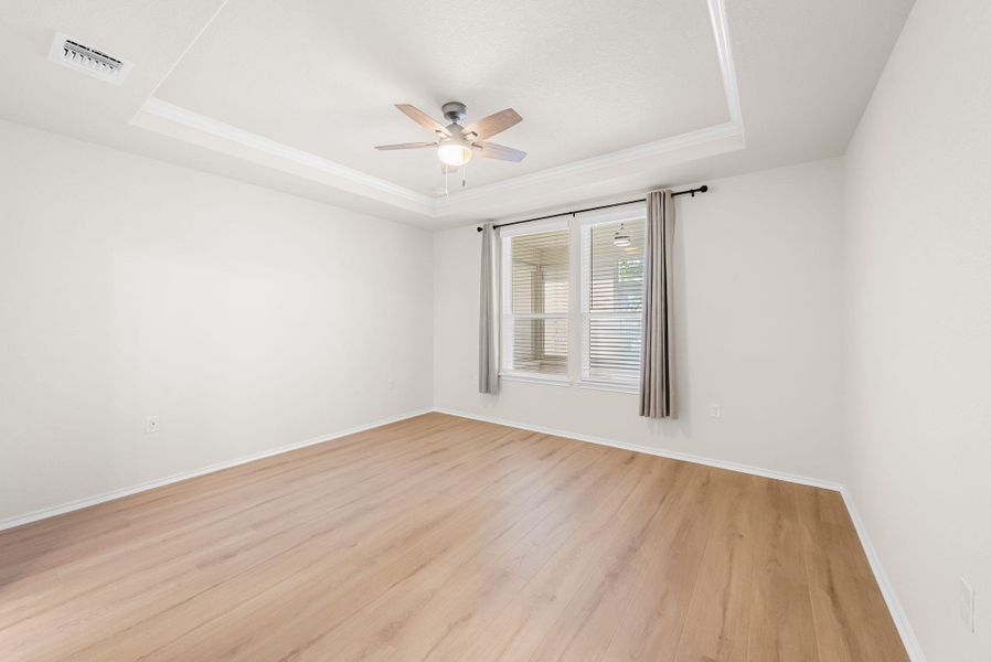 A well-lit bedroom features a decorative tray ceiling with a modern fan and light wood flooring. A well-lit bedroom features a decorative tray ceiling with a modern fan and light wood flooring.