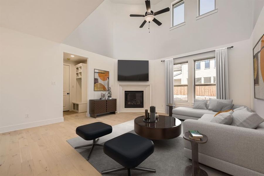 Virtually Staged Photo - Living area with plenty of natural light, light wood finished floors, a glass covered fireplace, a ceiling fan, and a high ceiling