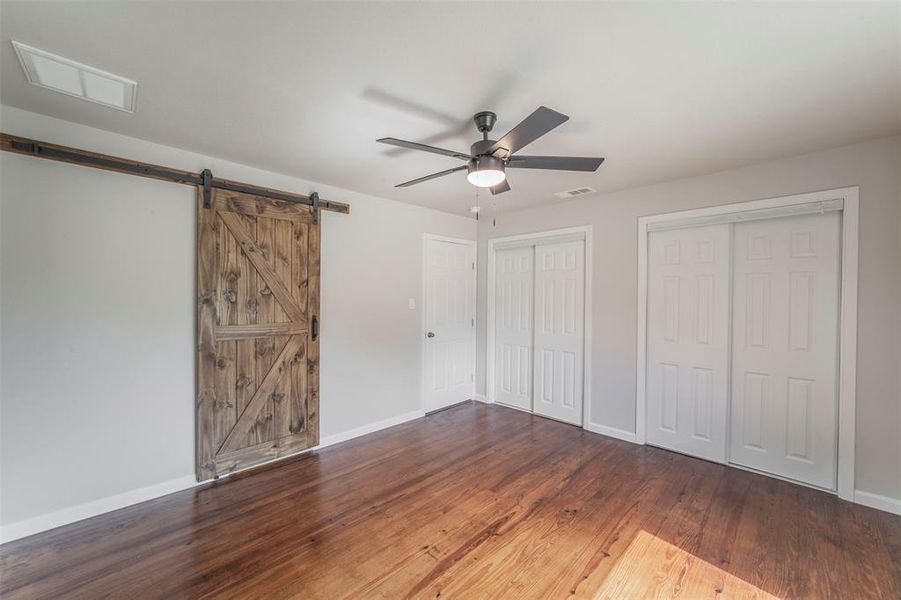 Primary bedroom with a barn door, ceiling fan, and hardwood / wood-style floors