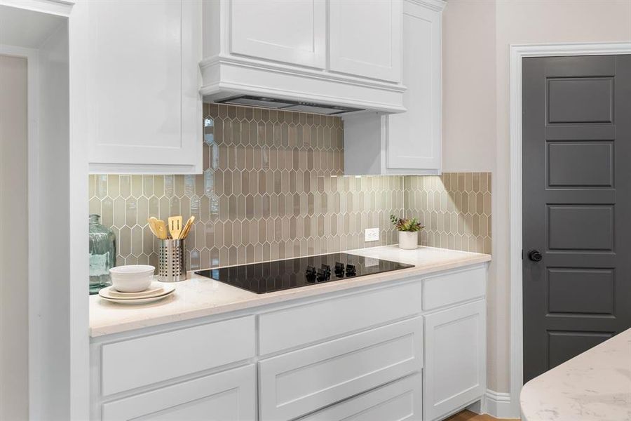 Kitchen with black electric cooktop, tasteful backsplash, white cabinets, and custom exhaust hood