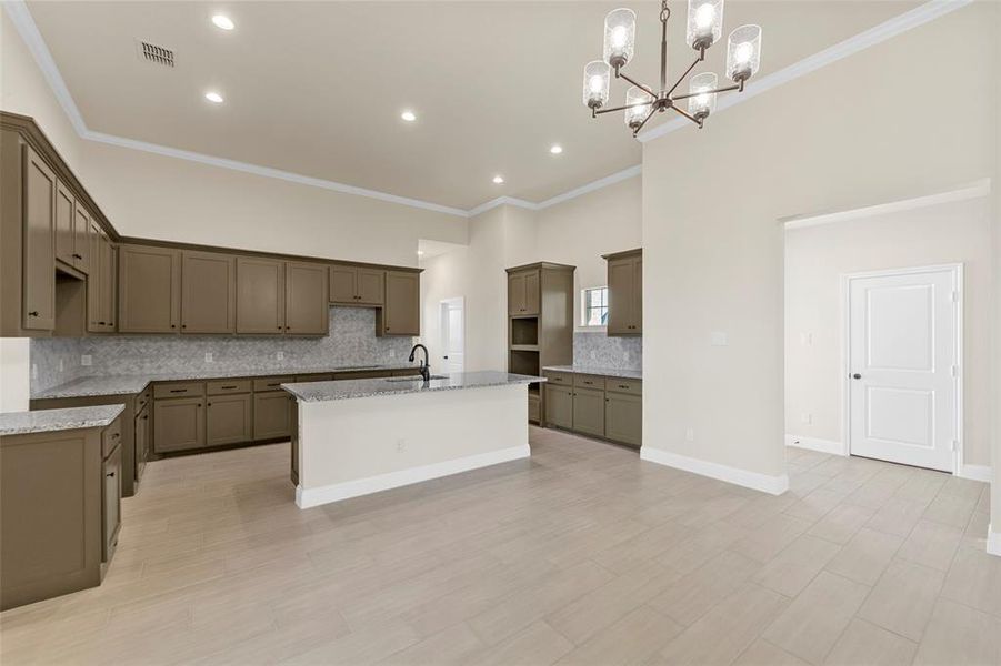 Kitchen featuring decorative backsplash, light stone counters, suspended lighting, an island with sink, and open floor plan Kitchen featuring decorative backsplash, light stone counters, suspended lighting, an island with sink, and open floor plan