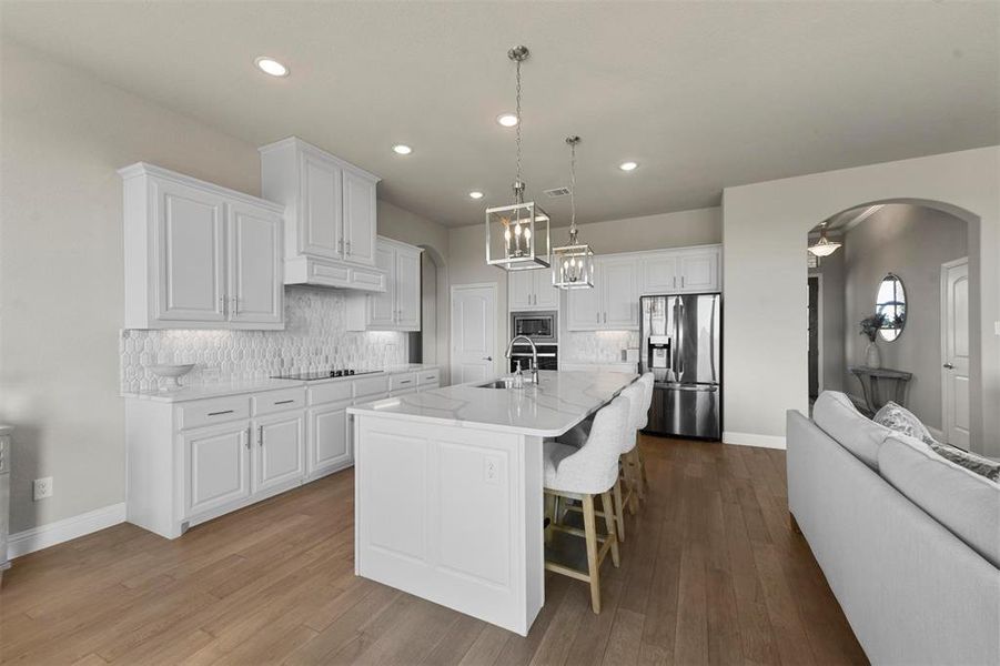 Kitchen featuring white cabinets, backsplash, stainless steel appliances, and an island with sink