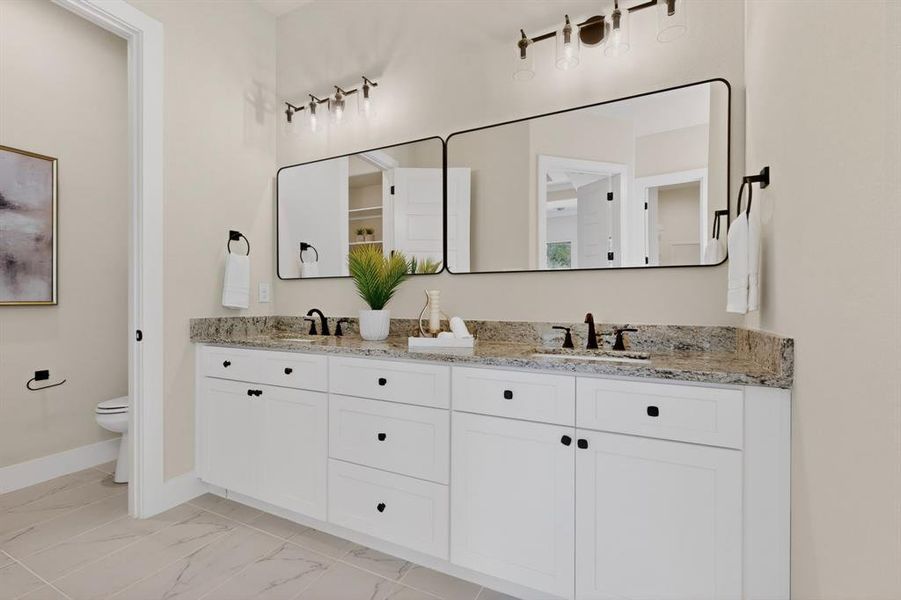 Dual vanity featuring white shaker cabinetry with dark hardware, a light-toned stone countertop, and two rectangular framed mirrors