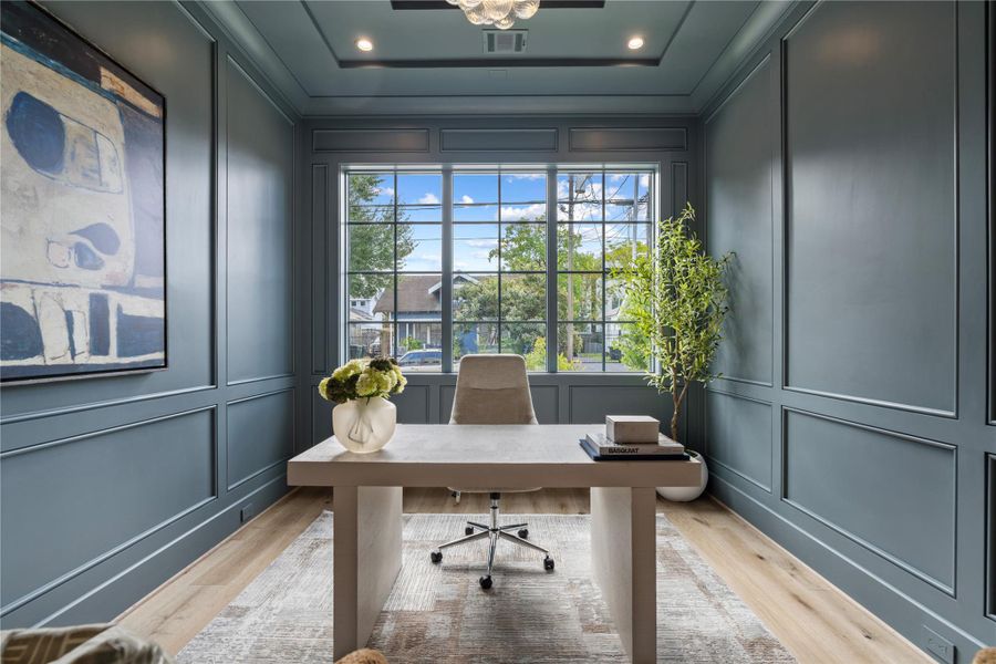 The front office showcases a stepped tray ceiling and wainscoting throughout. The medium gray tones parallel those of the exterior of the home and offer an elevated atmosphere. These big windows will keep you awake while you work from home!