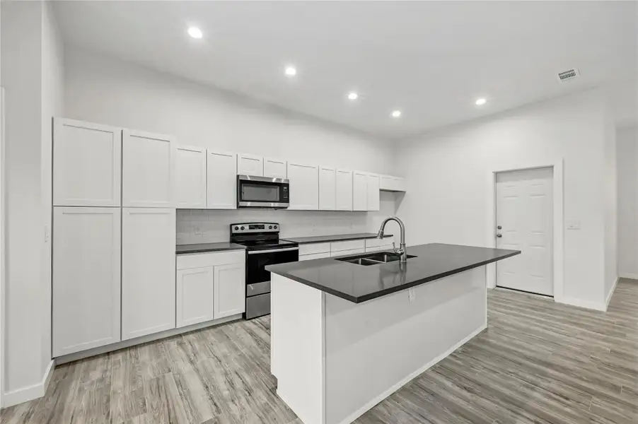 Kitchen with stainless steel appliances, white cabinets, an island with sink, dark countertops, and backsplash
