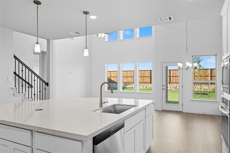 Kitchen with white cabinetry, hanging light fixtures, appliances with stainless steel finishes, a chandelier, and light stone countertops Kitchen with white cabinetry, hanging light fixtures, appliances with stainless steel finishes, a chandelier, and light stone countertops