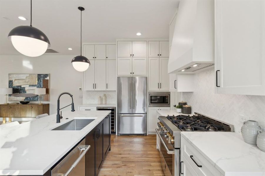 Kitchen with sink, white cabinetry, custom range hood, hanging light fixtures, and high quality appliances