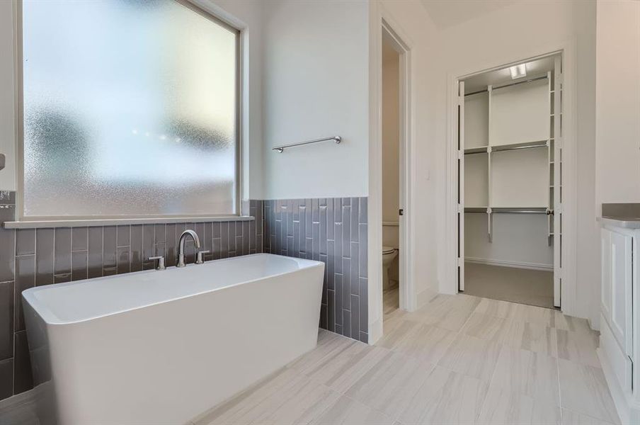 Bathroom featuring a washtub, tile walls, vanity, and toilet