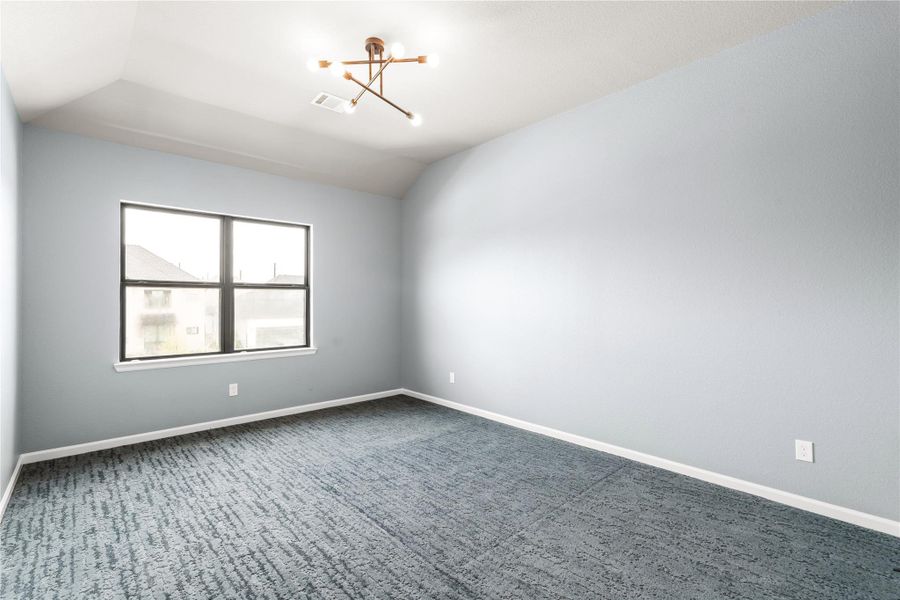 Spacious secondary bedroom with plush carpeting, enhanced by a modern light fixture and a large window providing ample natural light.