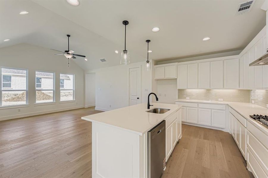 Kitchen with backsplash, white cabinetry, light wood-type flooring, lofted ceiling, and dishwasher Kitchen with backsplash, white cabinetry, light wood-type flooring, lofted ceiling, and dishwasher