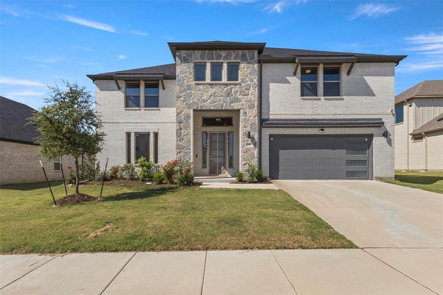 View of front of home featuring brick siding, a front yard, a garage, and concrete driveway