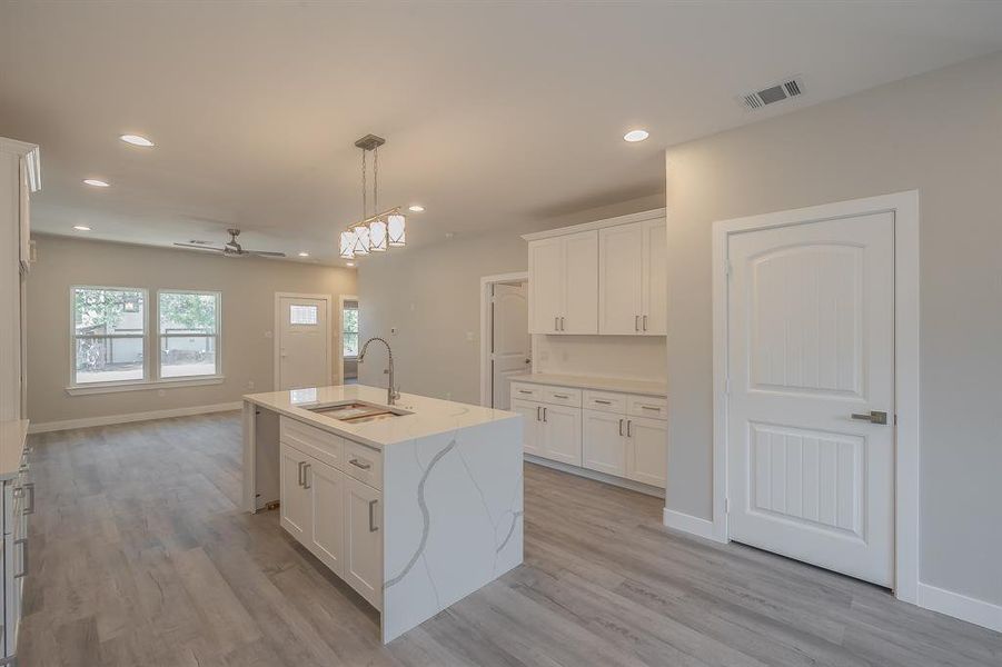 Kitchen featuring ceiling fan, hanging light fixtures, a kitchen island with sink, white cabinetry, and recessed lighting