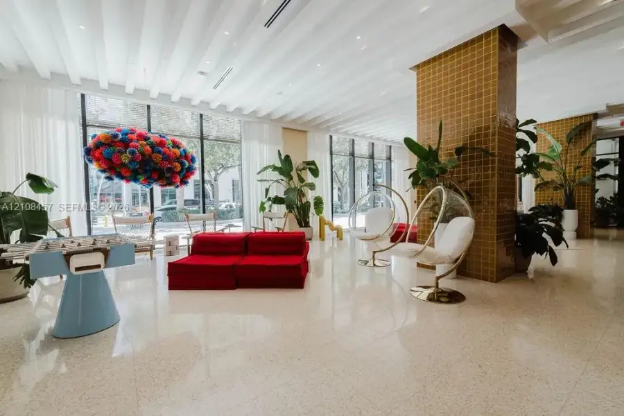 Spacious common area featuring floor-to-ceiling glass windows, recessed ceiling lighting, light-toned stone-finish flooring, and a structural column with mustard-colored tile cladding Spacious common area featuring floor-to-ceiling glass windows, recessed ceiling lighting, light-toned stone-finish flooring, and a structural column with mustard-colored tile cladding