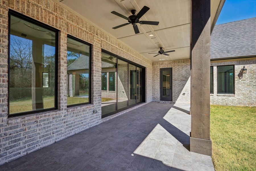 This photo showcases a covered patio with ceiling fans, large sliding glass doors, and a brick exterior. It offers a spacious area for outdoor relaxation, overlooking a grassy yard.