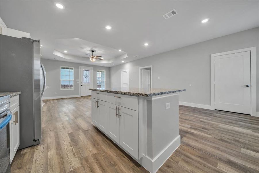 Kitchen with stone counters, a kitchen island, stainless steel refrigerator, white cabinetry, and a raised ceiling