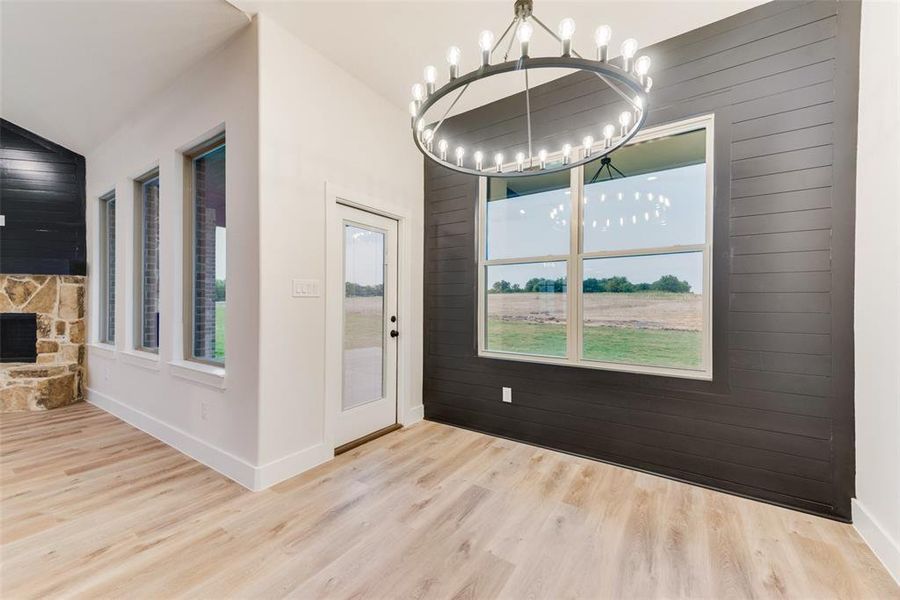 Unfurnished dining area featuring wooden walls, light wood finished floors, a fireplace, a chandelier, and lofted ceiling Unfurnished dining area featuring wooden walls, light wood finished floors, a fireplace, a chandelier, and lofted ceiling