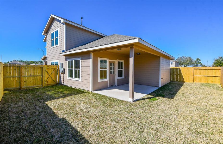 A two-story beige house with a covered patio and a wooden fence around a backyard on a clear day.