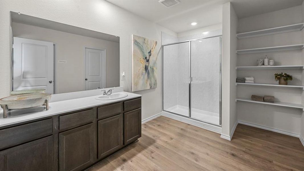 Bathroom with double vanity, a shower stall, and light wood-type flooring
