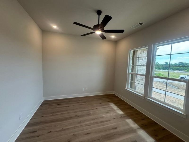 Spacious room featuring wood-finish flooring, a contemporary ceiling fan, recessed lighting, and two large windows with white trim Spacious room featuring wood-finish flooring, a contemporary ceiling fan, recessed lighting, and two large windows with white trim