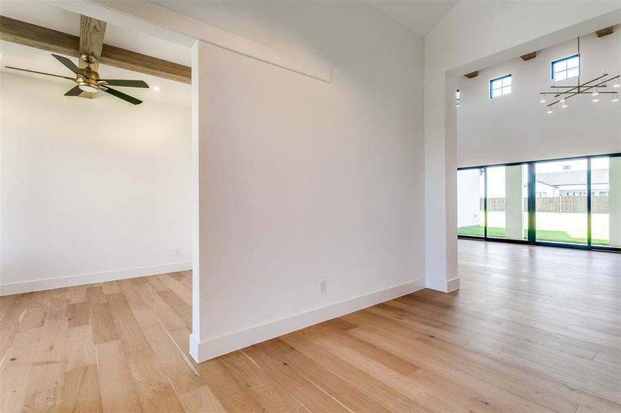 Empty room with light wood-style flooring, a ceiling fan, beamed ceiling, and a towering ceiling