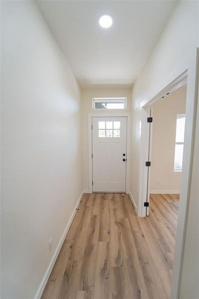 Inviting entryway featuring wood-finish flooring, a white paneled door with windowpanes, and an overhead transom window-offers easy access to flex room