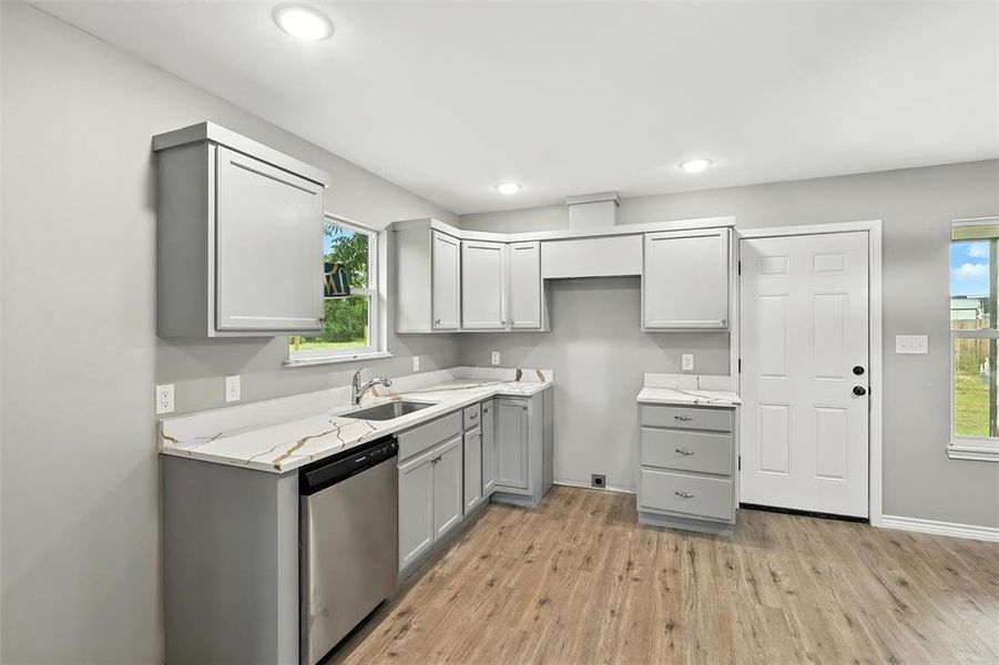 Kitchen with gray cabinets, dishwasher, light wood finished floors, light stone counters, and recessed lighting Kitchen with gray cabinets, dishwasher, light wood finished floors, light stone counters, and recessed lighting