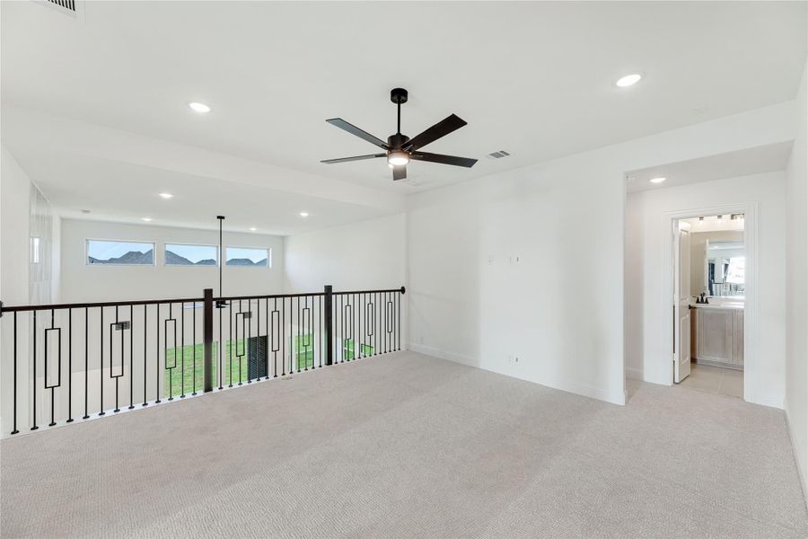 Open upstairs loft with carpet, ceiling fan, black metal railing, and doorway to bathroom