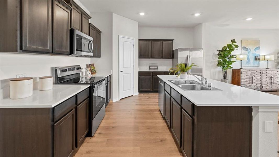 The kitchen features dark wood cabinetry, stainless steel appliances, and light-colored countertops The kitchen features dark wood cabinetry, stainless steel appliances, and light-colored countertops
