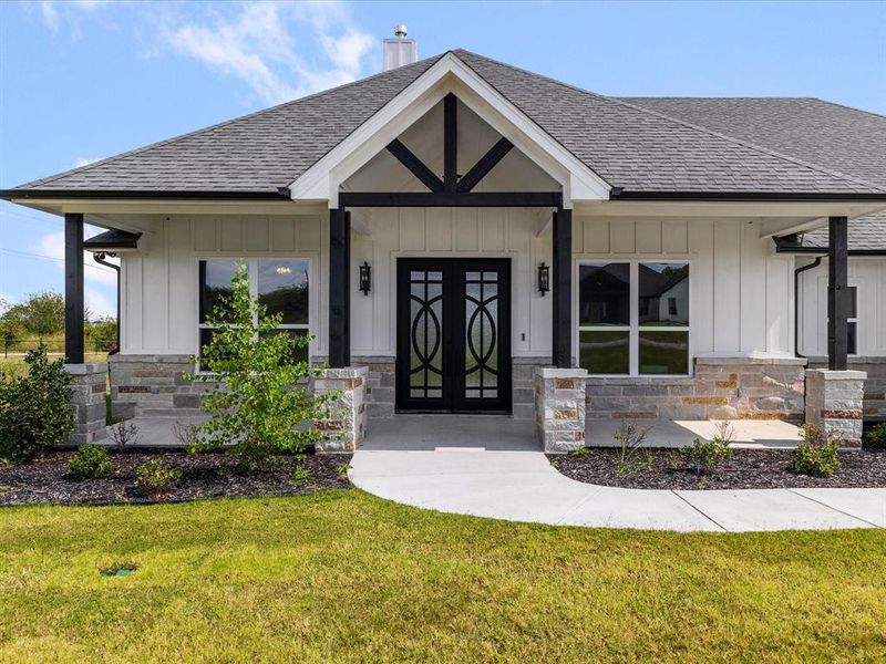Doorway to property with a shingled roof, a yard, board and batten siding, and stone siding Doorway to property with a shingled roof, a yard, board and batten siding, and stone siding