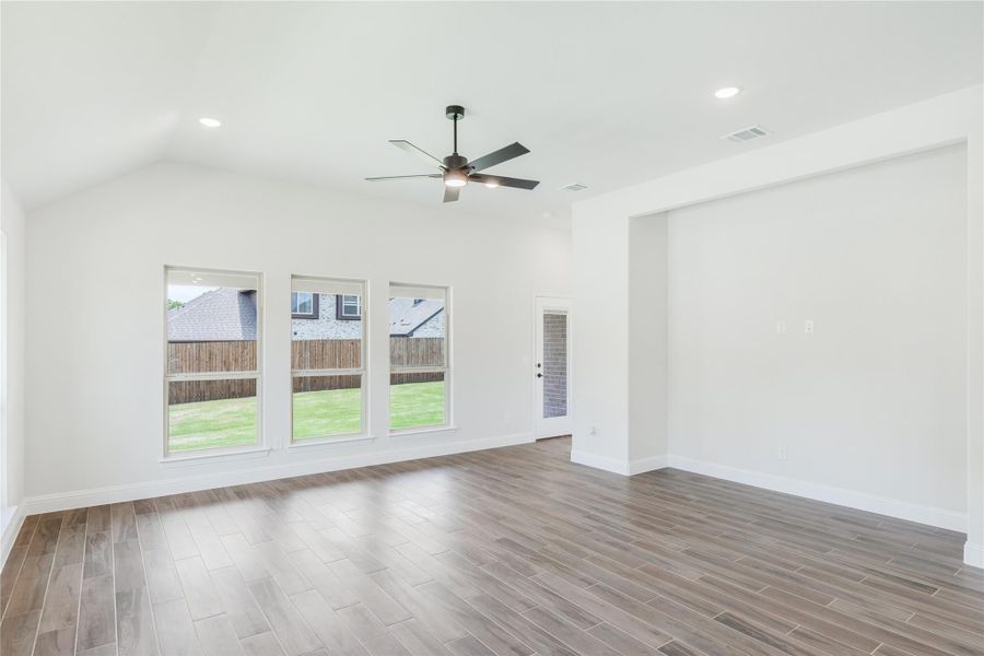 Open living room with vaulted ceiling, ceiling fan, wood-look floors, and large windows overlooking backyard Open living room with vaulted ceiling, ceiling fan, wood-look floors, and large windows overlooking backyard