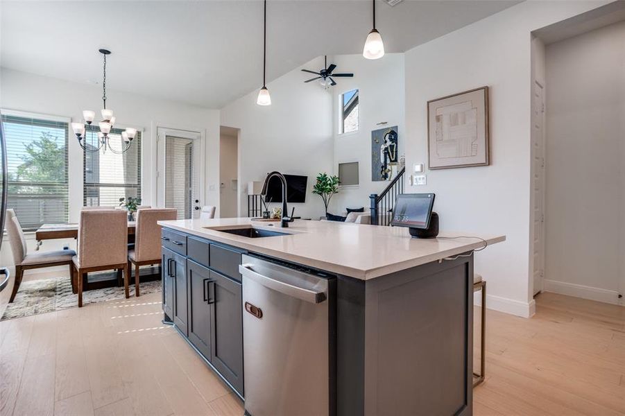 Kitchen featuring vaulted ceiling, stainless steel dishwasher, ceiling fan, light wood-type flooring, and a center island with sink
